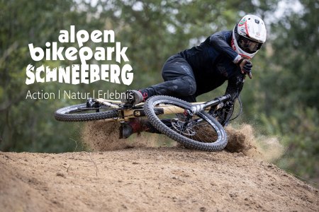 Mountainbiker in schwarzer Schutzkleidung und Helm f&auml;hrt in Kurve auf Dirt-Trail im Alpen Bikepark Schneeberg.
